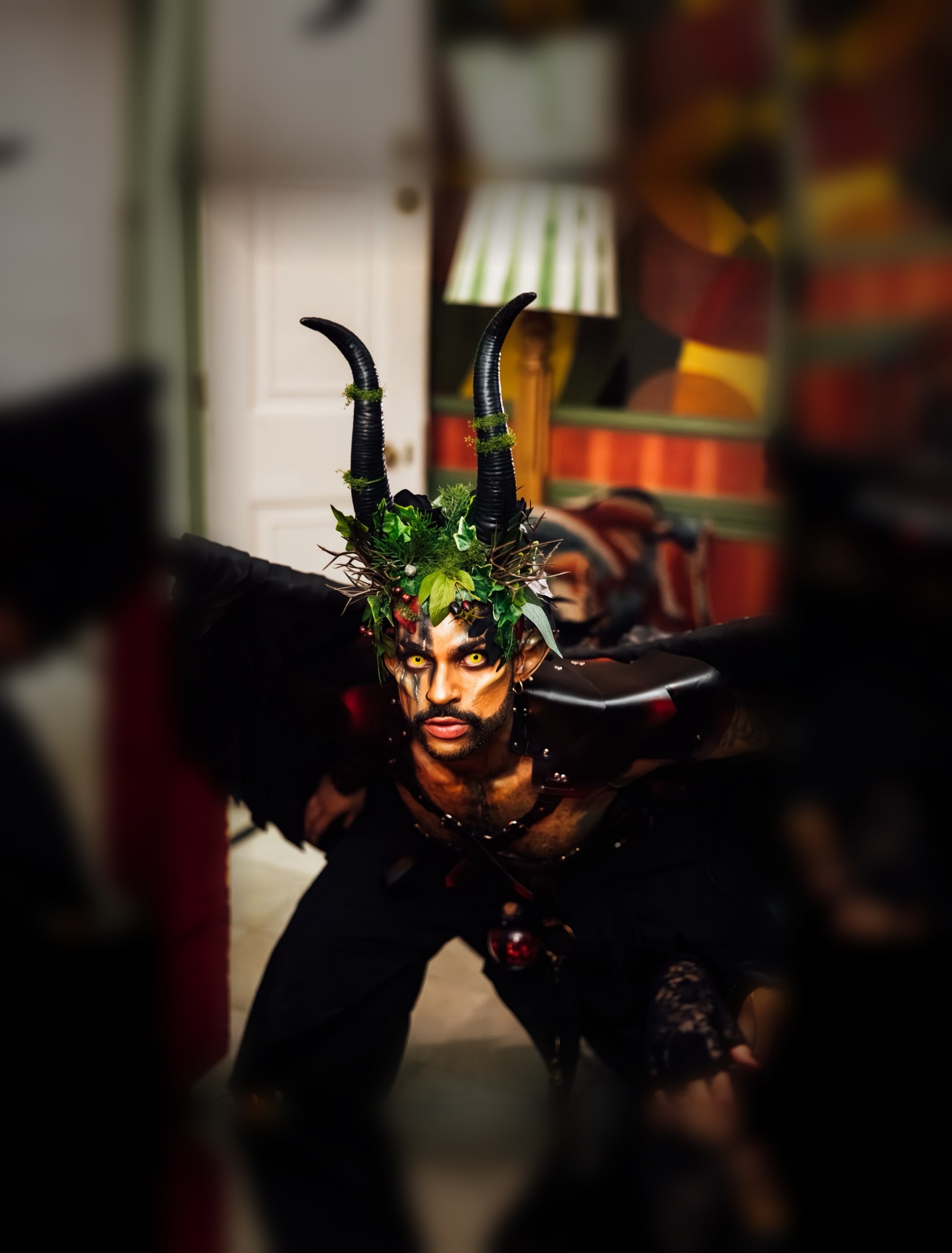 A horned creature wearing a crown of leaves and berries, black wings spread, glowing yellow eyes